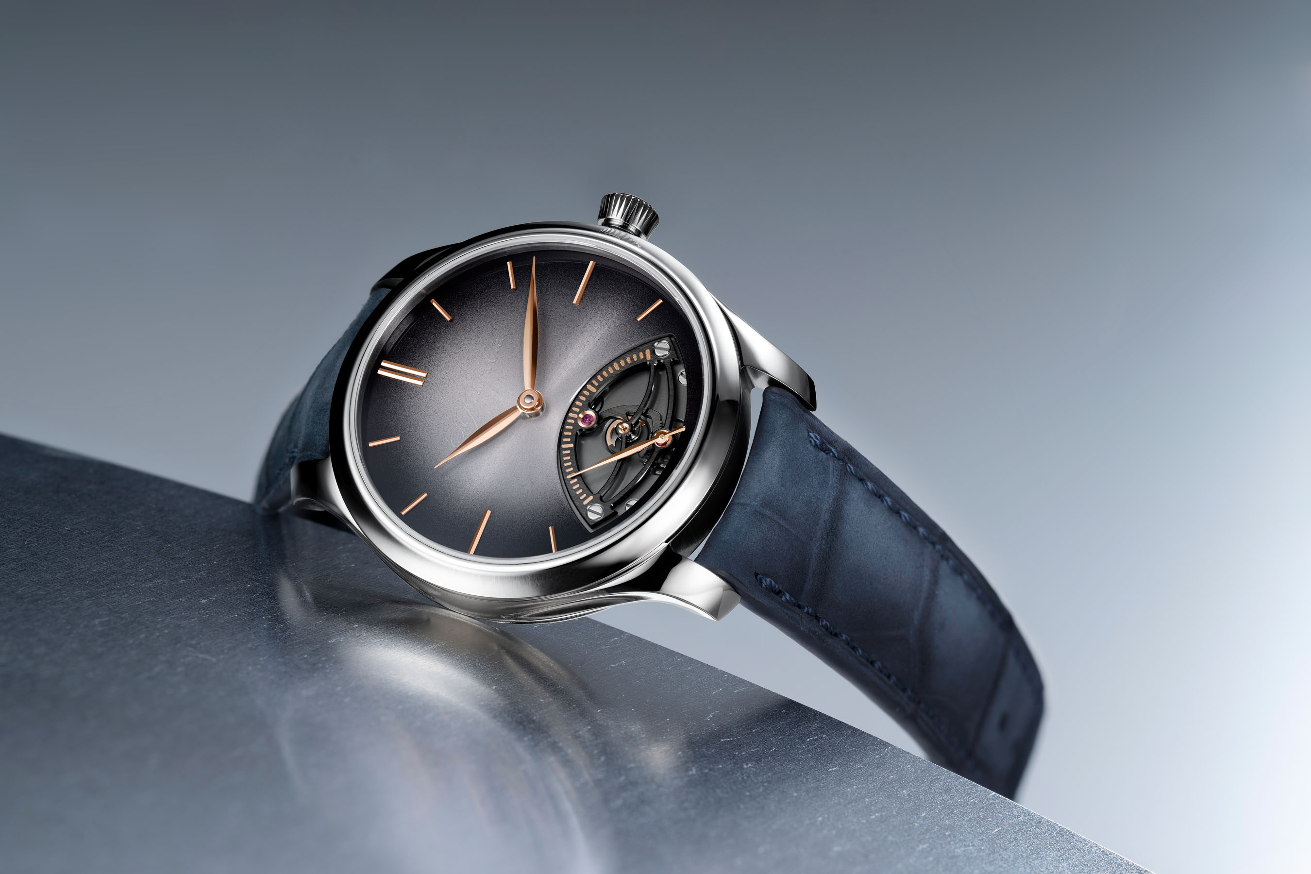 H. Moser & Cie. Endeavour Retrograde Seconds with a smoky Blackor fume dial and night blue strap resting on a curved steel surface